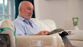 Elderly male patient with oxygen concentrator reading magazine at home
